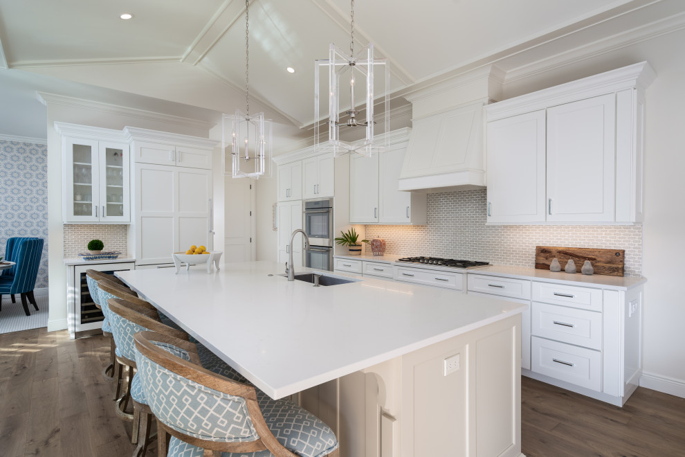 Example of a large beach style l-shaped light wood floor and beige floor open concept kitchen design in Other with an undermount sink, shaker cabinets, quartz countertops, beige backsplash, marble backsplash, paneled appliances, an island and white countertops