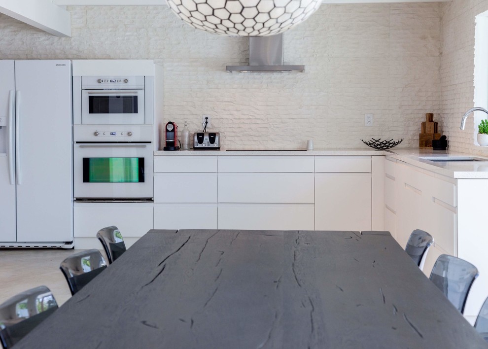 Bild på ett funkis kök, med en dubbel diskho, släta luckor, vita skåp, bänkskiva i kvarts, vitt stänkskydd, stänkskydd i stenkakel, vita vitvaror och betonggolv