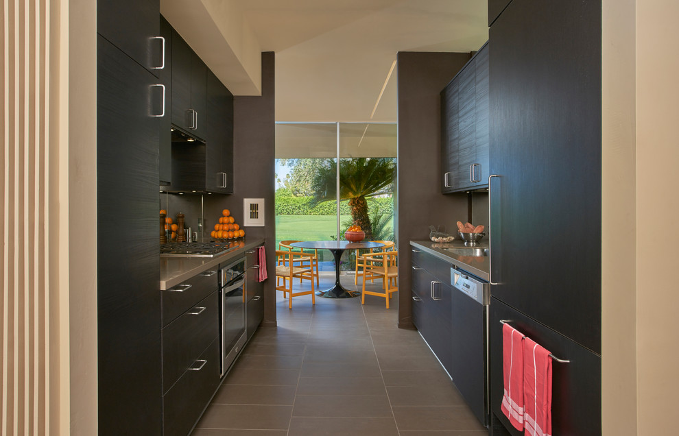 Exemple d'une petite cuisine parallèle rétro en bois foncé avec un placard à porte plane, une crédence miroir, un électroménager en acier inoxydable, un sol en carrelage de porcelaine, aucun îlot et un sol marron.