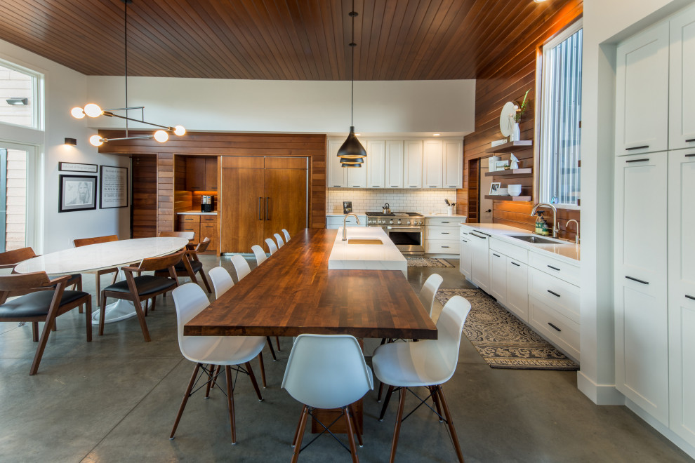 This is an example of a large contemporary l-shaped kitchen/diner in Other with a submerged sink, white splashback, wood splashback, concrete flooring, an island, white worktops, shaker cabinets, white cabinets, stainless steel appliances and grey floors.