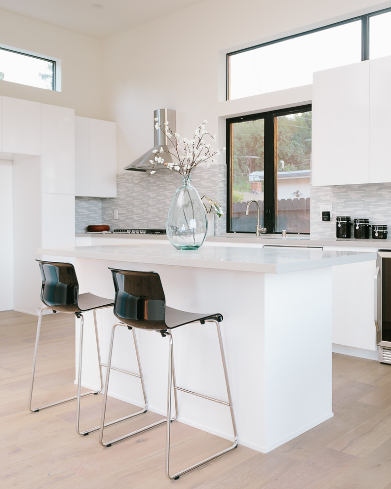 Moderne Küche mit flächenbündigen Schrankfronten, weißen Schränken, bunter Rückwand, hellem Holzboden und Kücheninsel in Los Angeles