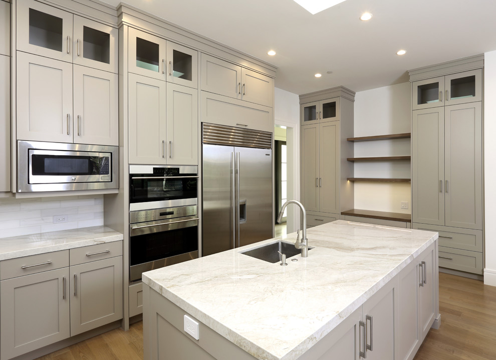 Modern inredning av ett stort kök, med en undermonterad diskho, skåp i shakerstil, grå skåp, marmorbänkskiva, vitt stänkskydd, stänkskydd i stenkakel, rostfria vitvaror, ljust trägolv och flera köksöar