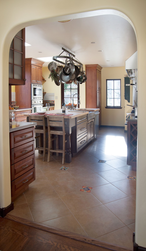 Large tuscan u-shaped ceramic tile enclosed kitchen photo in San Francisco with a farmhouse sink, raised-panel cabinets, dark wood cabinets, stainless steel countertops, multicolored backsplash, ceramic backsplash, stainless steel appliances and an island
