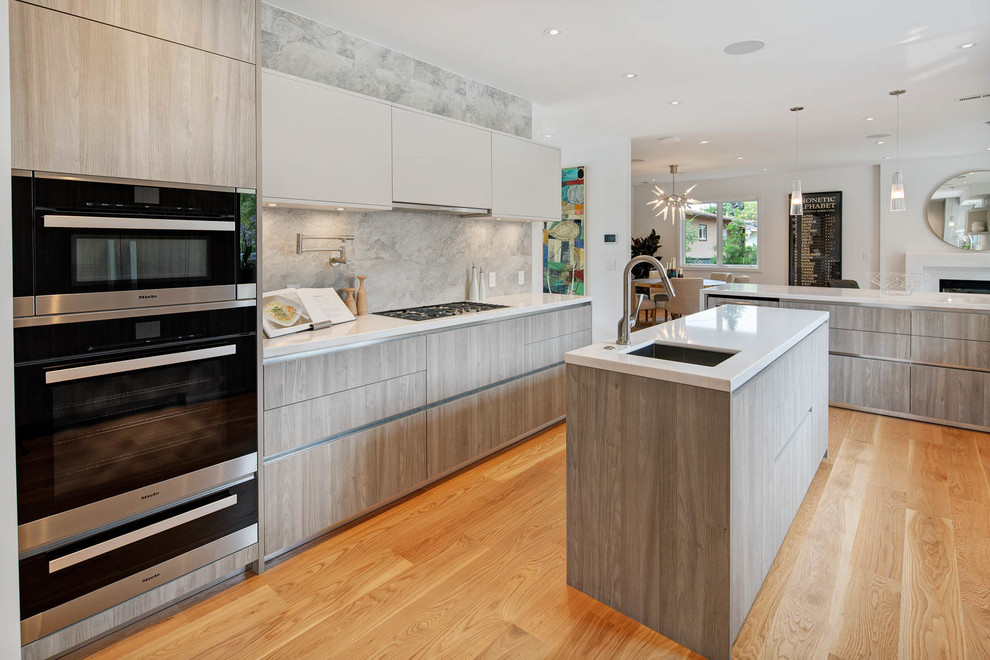 Example of a trendy medium tone wood floor and brown floor open concept kitchen design in San Francisco with an undermount sink, flat-panel cabinets, gray cabinets, gray backsplash, black appliances, two islands and white countertops