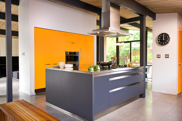Example of a mid-sized minimalist single-wall concrete floor and gray floor eat-in kitchen design in San Francisco with flat-panel cabinets, orange cabinets, stainless steel countertops, stainless steel appliances, an island and gray countertops