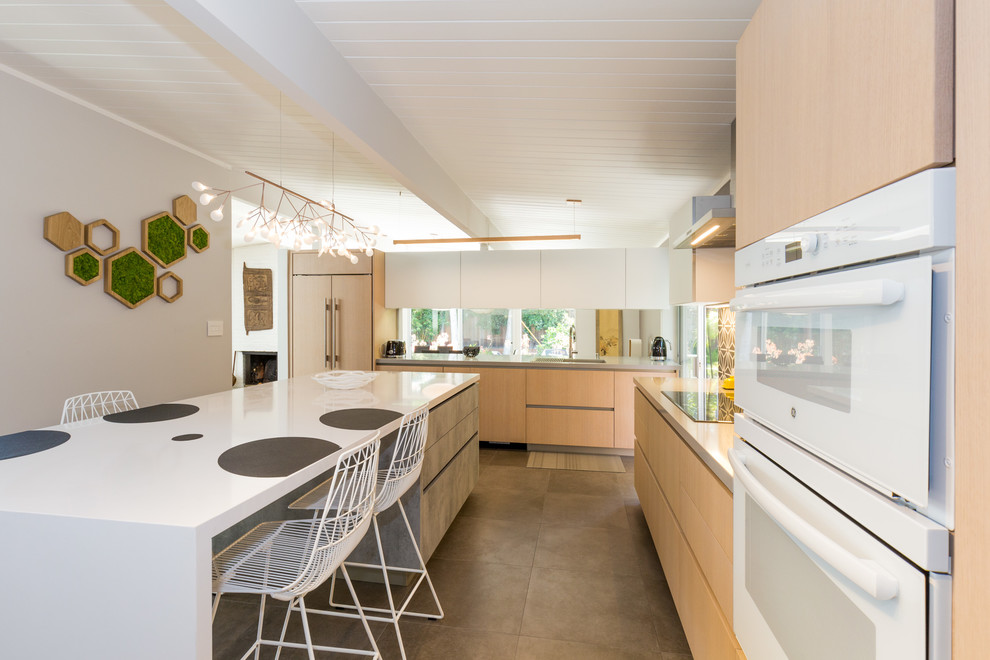 Photo of a medium sized modern l-shaped enclosed kitchen in San Francisco with a submerged sink, flat-panel cabinets, light wood cabinets, engineered stone countertops, grey splashback, ceramic splashback, white appliances, concrete flooring, an island and grey floors.