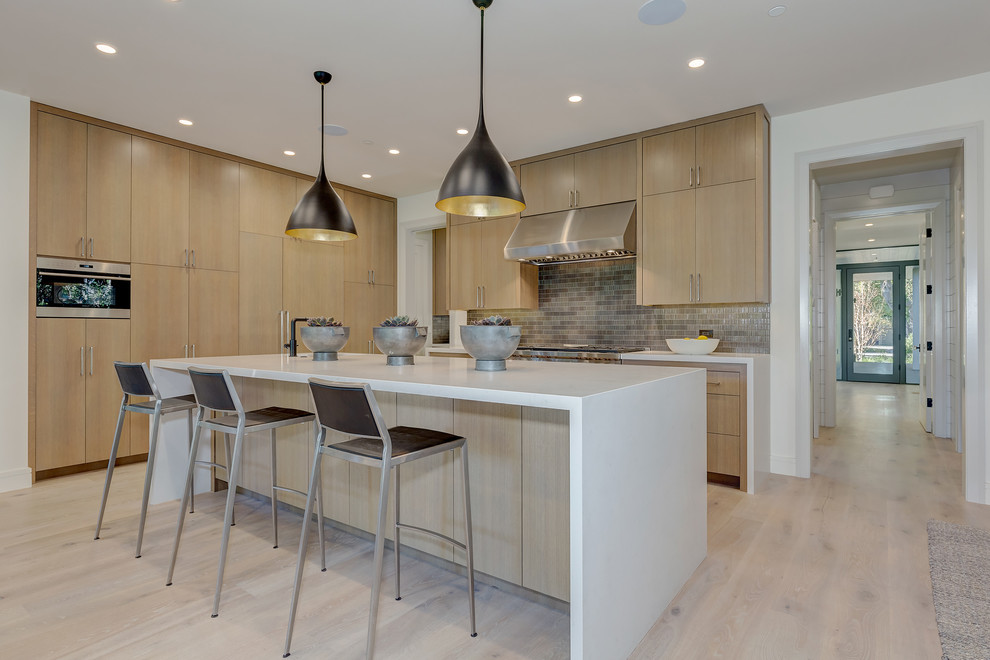 Immagine di una cucina design con ante lisce, ante in legno chiaro, parquet chiaro, paraspruzzi grigio, elettrodomestici in acciaio inossidabile e pavimento beige