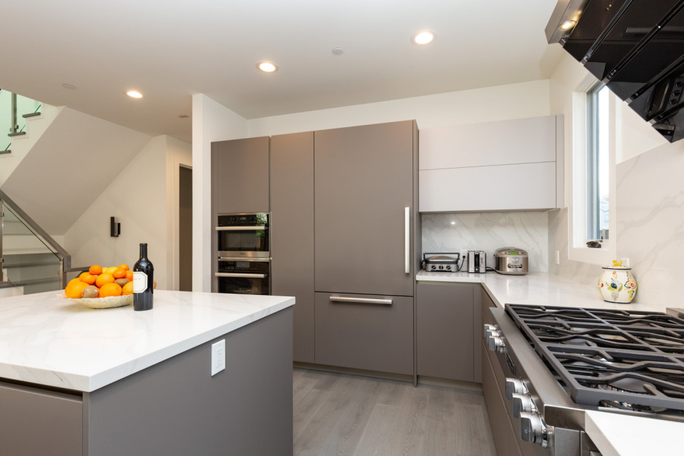 Modern inredning av ett stort grå grått kök, med en undermonterad diskho, släta luckor, bruna skåp, bänkskiva i glas, grått stänkskydd, rostfria vitvaror, en köksö och grått golv