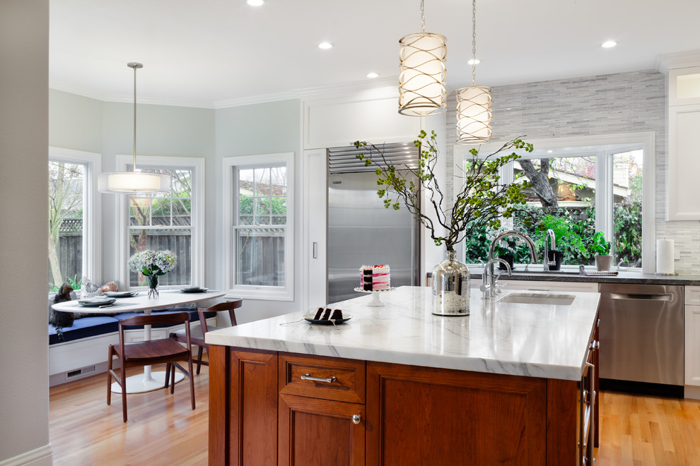 This is an example of a large classic u-shaped kitchen/diner in San Francisco with a built-in sink, glass-front cabinets, white cabinets, marble worktops, grey splashback, stone tiled splashback, stainless steel appliances, medium hardwood flooring and an island.