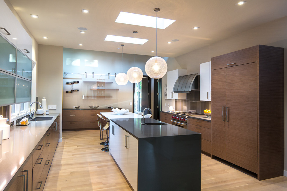Large contemporary galley enclosed kitchen in San Francisco with flat-panel cabinets, medium wood cabinets, engineered stone countertops, grey splashback, an island, stainless steel appliances, light hardwood flooring, an integrated sink, porcelain splashback and beige floors.