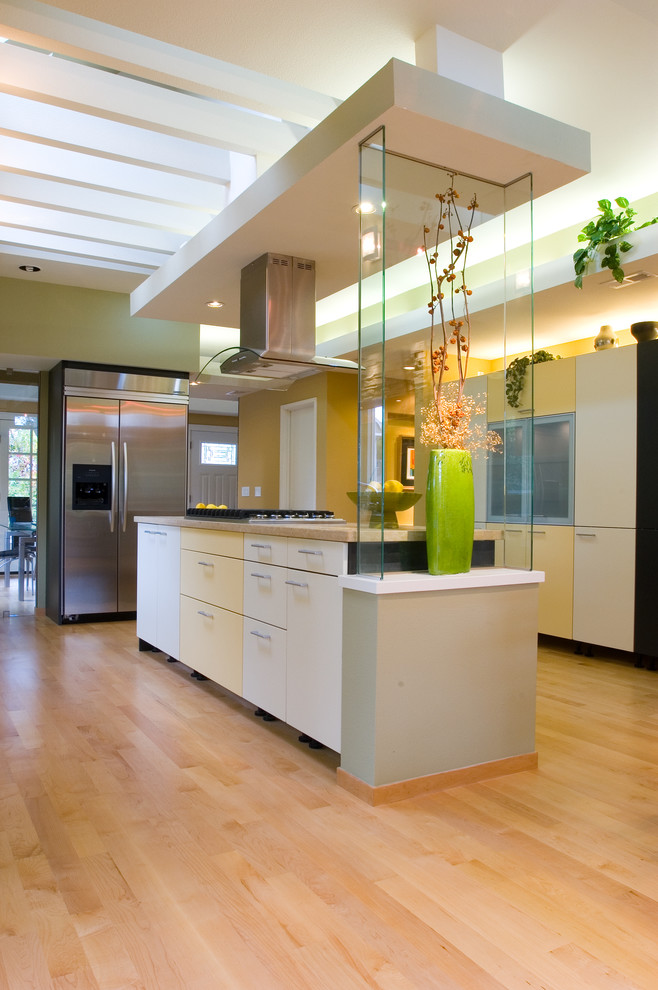 Bild på ett funkis kök, med en undermonterad diskho, släta luckor, gula skåp, bänkskiva i kalksten, stänkskydd i glaskakel, rostfria vitvaror, mellanmörkt trägolv och en köksö