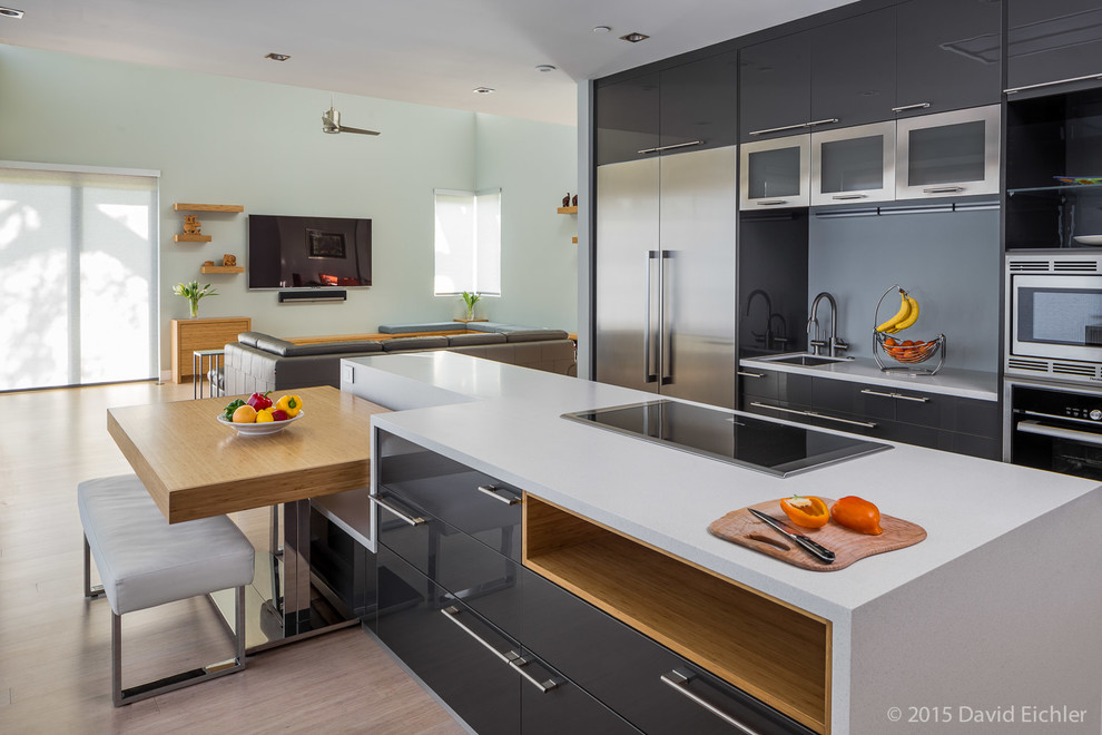 Immagine di una cucina minimalista con ante lisce, ante grigie, top in superficie solida, elettrodomestici in acciaio inossidabile e parquet chiaro
