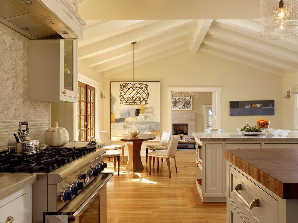Inredning av ett klassiskt stort kök, med rostfria vitvaror, träbänkskiva, grått stänkskydd, luckor med infälld panel, vita skåp, stänkskydd i stenkakel, mellanmörkt trägolv, en köksö och brunt golv