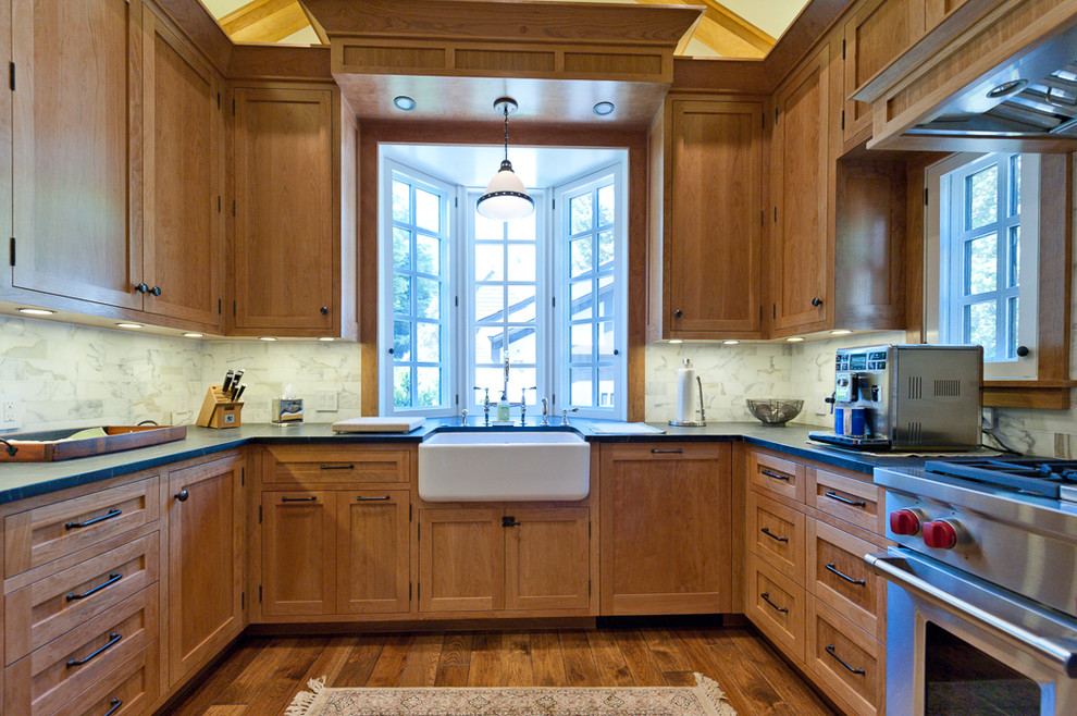 Example of a mid-sized classic u-shaped dark wood floor and brown floor enclosed kitchen design in San Francisco with a farmhouse sink, shaker cabinets, medium tone wood cabinets, soapstone countertops, white backsplash, marble backsplash, stainless steel appliances and no island