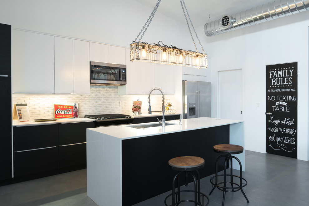 Foto på ett industriellt kök, med en undermonterad diskho, släta luckor, vita skåp, vitt stänkskydd, rostfria vitvaror, betonggolv, en köksö och grått golv