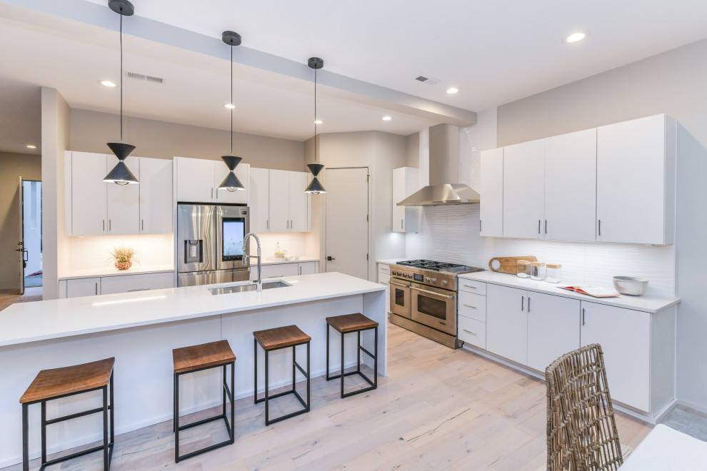 Mid-sized minimalist l-shaped beige floor open concept kitchen photo in Charlotte with an undermount sink, flat-panel cabinets, white cabinets, white backsplash, stainless steel appliances, an island and white countertops
