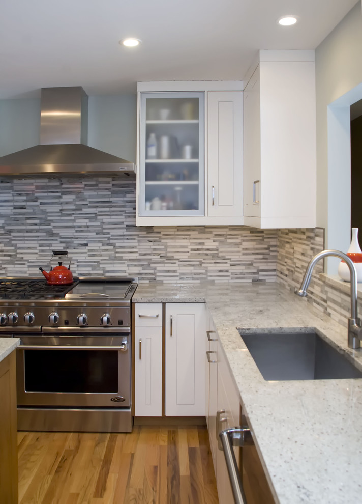 Inredning av ett modernt kök, med rostfria vitvaror, granitbänkskiva, en enkel diskho, vita skåp, grått stänkskydd och stänkskydd i stickkakel
