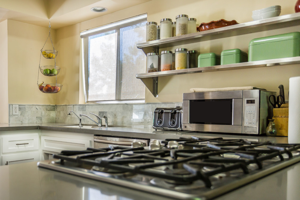 Modern inredning av ett kök, med en undermonterad diskho, luckor med infälld panel, vita skåp, flerfärgad stänkskydd, rostfria vitvaror, mörkt trägolv, en halv köksö, bänkskiva i kvartsit och stänkskydd i stenkakel