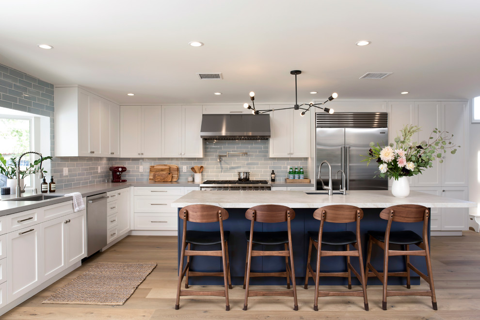 This is an example of a large classic l-shaped kitchen in Los Angeles with shaker cabinets, white cabinets, quartz worktops, blue splashback, stainless steel appliances, an island, grey worktops, a submerged sink, metro tiled splashback and light hardwood flooring.