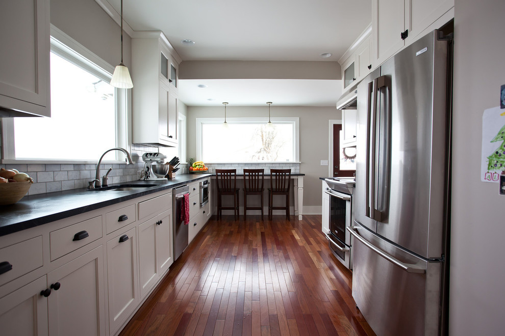 シアトルにある高級な広いトランジショナルスタイルのおしゃれなキッチン (アンダーカウンターシンク、シェーカースタイル扉のキャビネット、白いキャビネット、ソープストーンカウンター、グレーのキッチンパネル、石タイルのキッチンパネル、シルバーの調理設備、無垢フローリング、アイランドなし、茶色い床) の写真