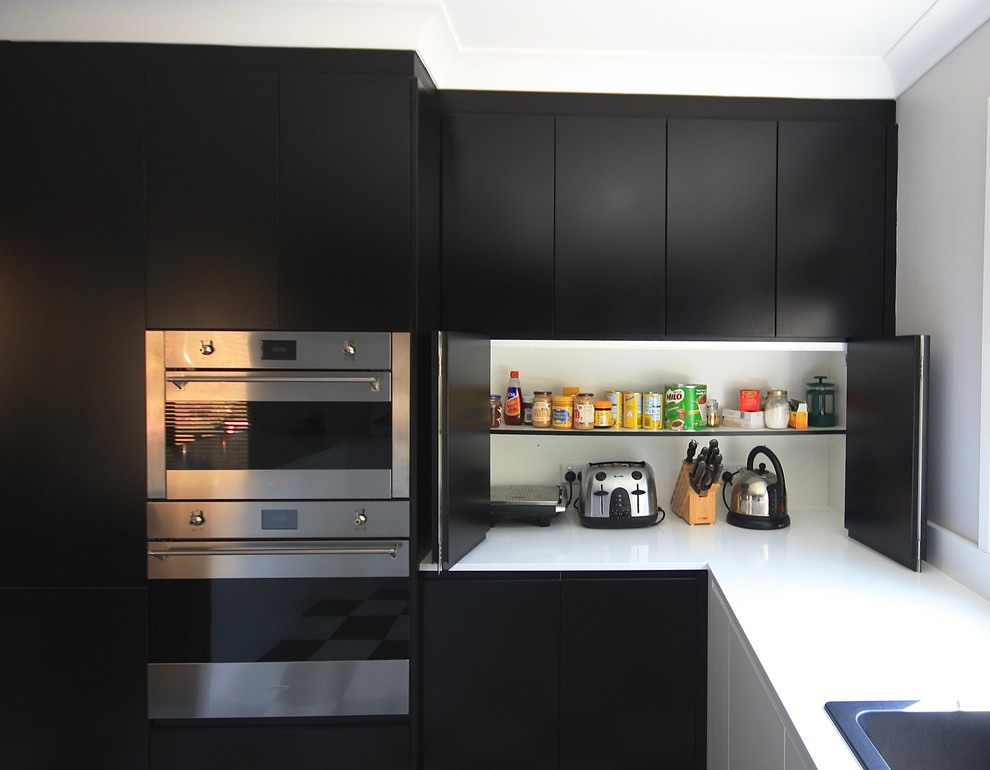 Modern inredning av ett avskilt, mellanstort u-kök, med en nedsänkt diskho, släta luckor, svarta skåp, bänkskiva i kvarts, vitt stänkskydd, stänkskydd i sten, svarta vitvaror, klinkergolv i keramik och svart golv
