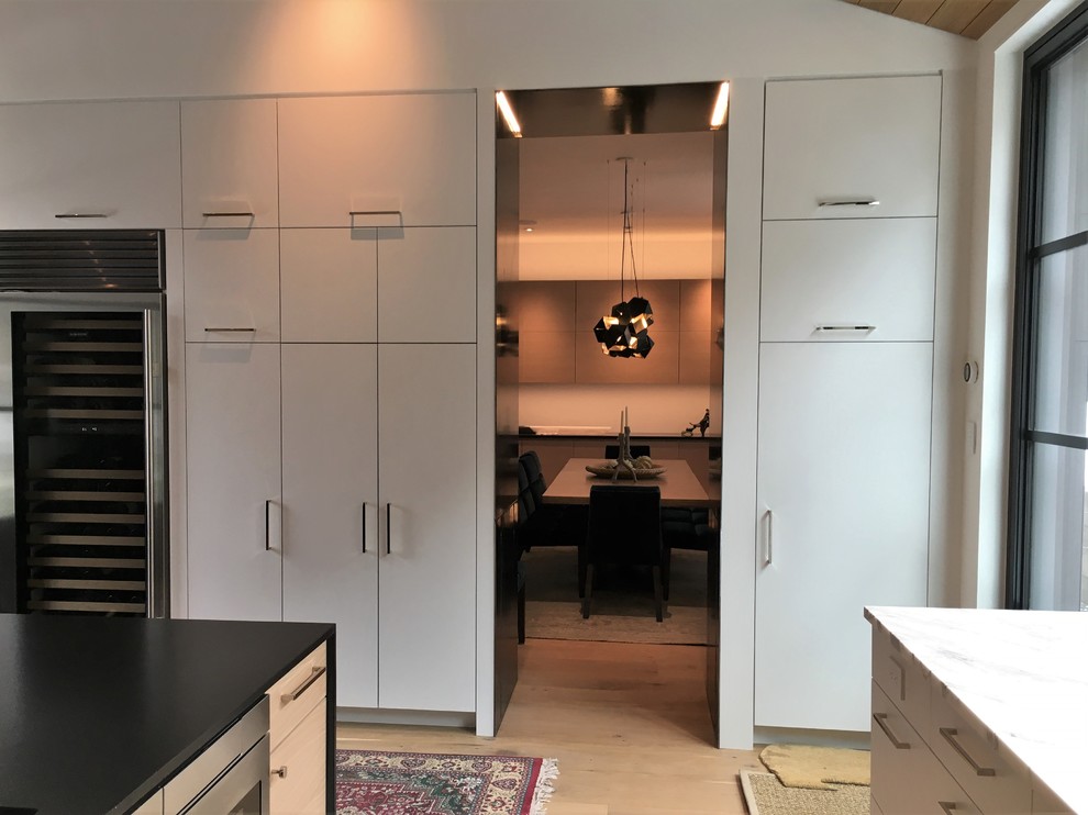 Example of a large trendy u-shaped light wood floor and beige floor enclosed kitchen design in Other with an undermount sink, flat-panel cabinets, white cabinets, marble countertops, white backsplash, marble backsplash, stainless steel appliances and an island