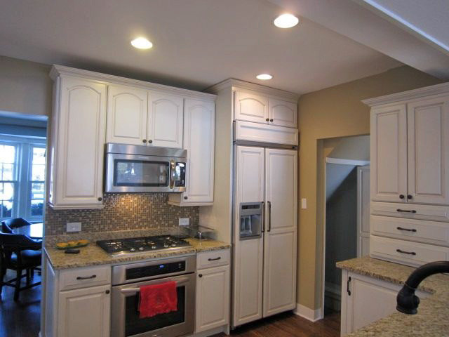 Cette image montre une cuisine américaine traditionnelle avec un placard à porte affleurante, des portes de placard blanches, un plan de travail en granite, une crédence en mosaïque et un électroménager en acier inoxydable.