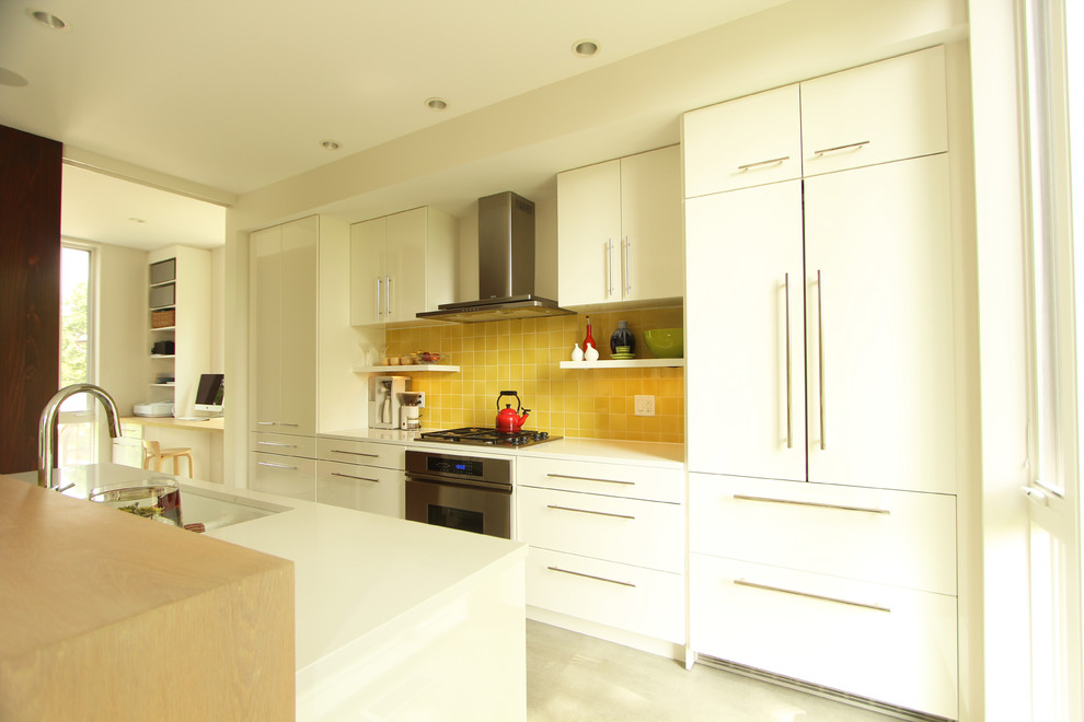 Bild på ett litet funkis linjärt kök med öppen planlösning, med en dubbel diskho, släta luckor, vita skåp, bänkskiva i kvarts, gult stänkskydd, stänkskydd i keramik, integrerade vitvaror, betonggolv och en köksö