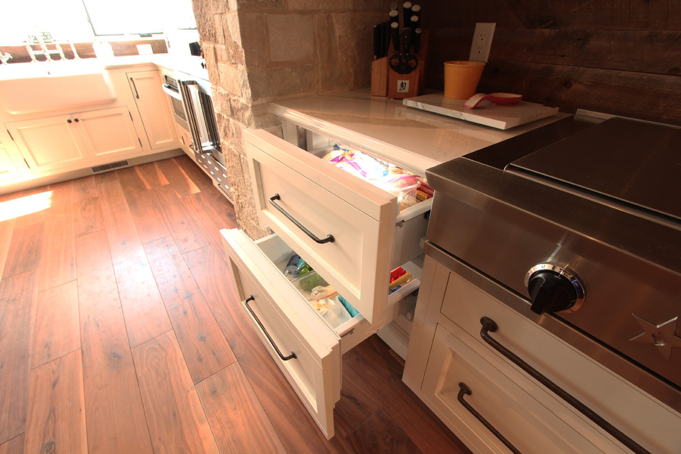 Photo of a large rural l-shaped open plan kitchen in Other with a belfast sink, recessed-panel cabinets, dark wood cabinets, engineered stone countertops, multi-coloured splashback, stone slab splashback, integrated appliances, medium hardwood flooring, multiple islands, brown floors and white worktops.