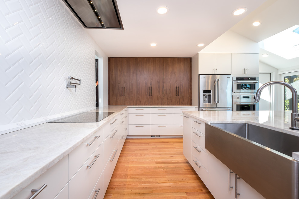 Example of a large transitional l-shaped medium tone wood floor open concept kitchen design in Portland with an undermount sink, flat-panel cabinets, white cabinets, quartzite countertops, white backsplash, ceramic backsplash, stainless steel appliances and an island