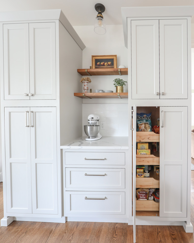 Bild på ett stort vintage vit vitt kök, med en undermonterad diskho, luckor med profilerade fronter, grå skåp, bänkskiva i kvartsit, vitt stänkskydd, stänkskydd i tunnelbanekakel, rostfria vitvaror, mellanmörkt trägolv och en köksö