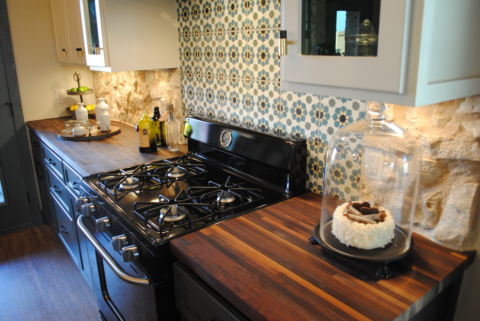 Exemple d'une cuisine éclectique avec un évier de ferme, des portes de placard blanches, un plan de travail en bois, un électroménager noir, un sol en vinyl et îlot.