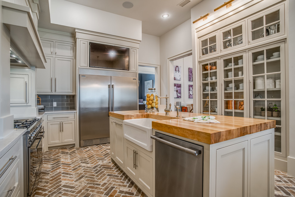 Kitchen - traditional brick floor kitchen idea in Austin with a farmhouse sink, quartzite countertops, porcelain backsplash, stainless steel appliances, an island and glass-front cabinets