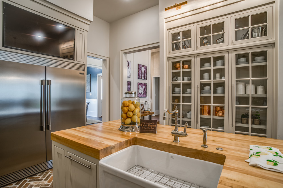 Photo of a rural kitchen in Austin with a belfast sink, shaker cabinets, quartz worktops, porcelain splashback, stainless steel appliances, brick flooring and an island.