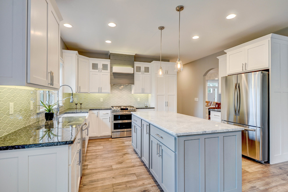 Photo of a traditional l-shaped kitchen in Milwaukee with a belfast sink, shaker cabinets, white cabinets, green splashback, stainless steel appliances, light hardwood flooring and an island.