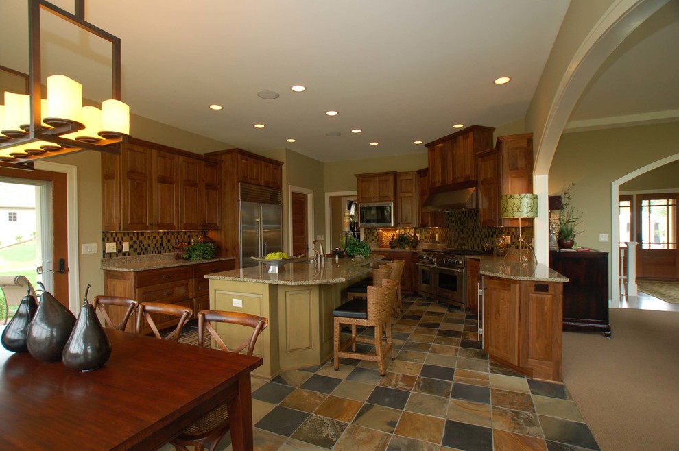 Large trendy u-shaped slate floor eat-in kitchen photo in Milwaukee with an undermount sink, raised-panel cabinets, dark wood cabinets, granite countertops, multicolored backsplash, glass tile backsplash, stainless steel appliances and two islands