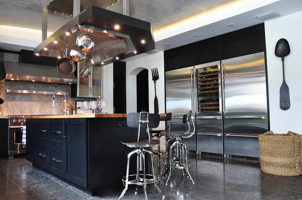 Large contemporary l-shaped kitchen/diner in Orlando with shaker cabinets, black cabinets, wood worktops, grey splashback, stainless steel appliances and limestone flooring.
