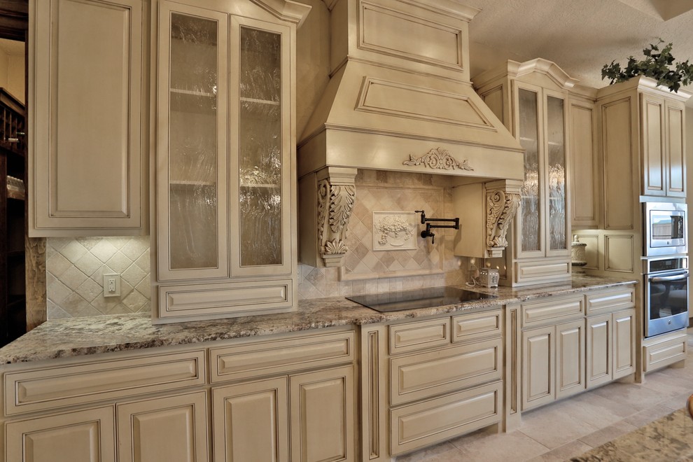 Example of a mid-sized tuscan porcelain tile eat-in kitchen design in Dallas with an undermount sink, shaker cabinets, distressed cabinets, granite countertops, beige backsplash, stone tile backsplash and stainless steel appliances