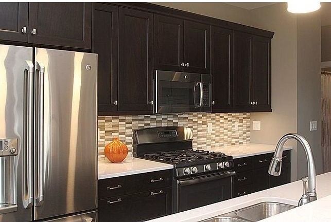 Example of a large trendy single-wall dark wood floor open concept kitchen design in Cedar Rapids with an undermount sink, shaker cabinets, dark wood cabinets, quartzite countertops, beige backsplash, mosaic tile backsplash, stainless steel appliances and an island