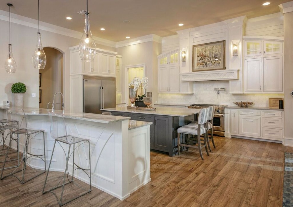 Example of a large transitional l-shaped medium tone wood floor and brown floor kitchen design in Austin with shaker cabinets, white cabinets, white backsplash, subway tile backsplash, stainless steel appliances and an island