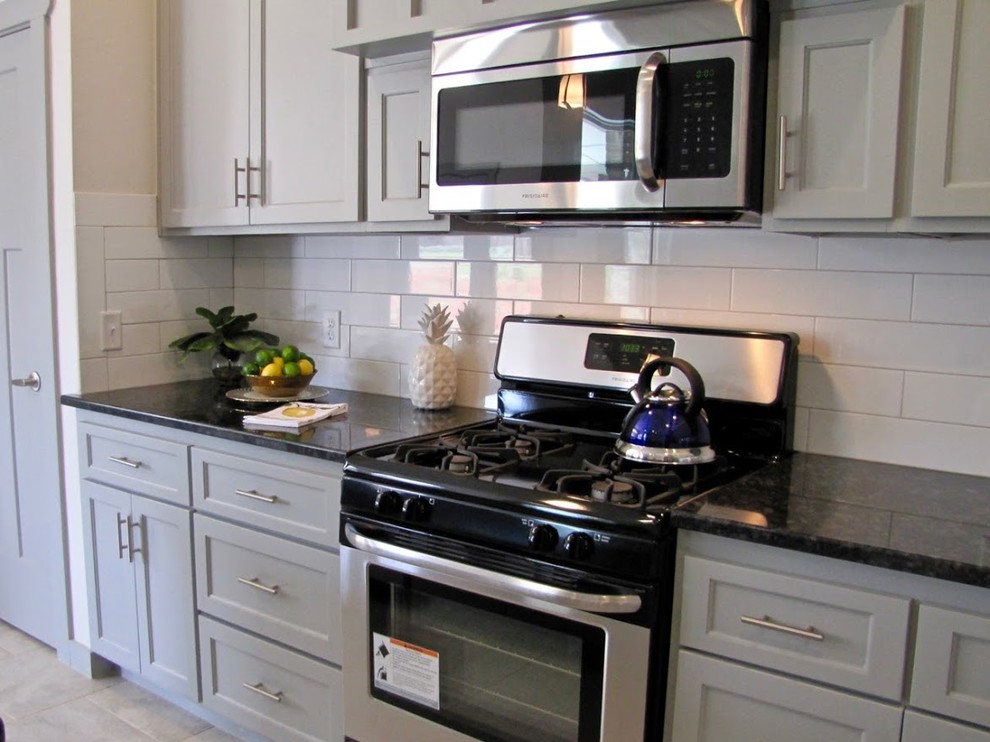 Example of a mid-sized transitional l-shaped ceramic tile and beige floor enclosed kitchen design in Oklahoma City with a double-bowl sink, gray cabinets, granite countertops, gray backsplash, subway tile backsplash, stainless steel appliances and an island