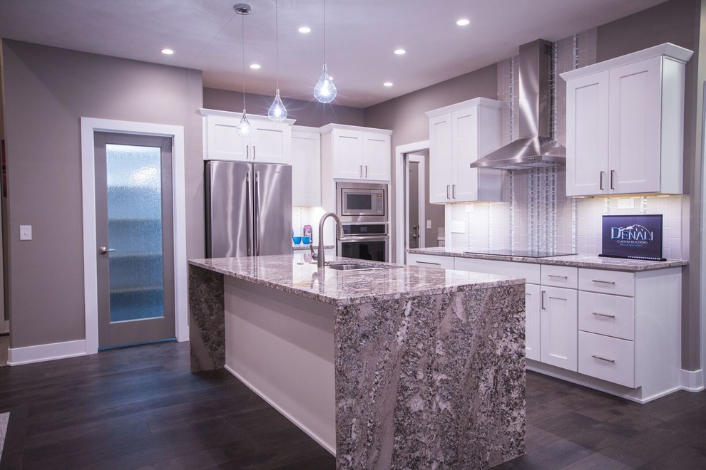 Open concept kitchen - mid-sized contemporary l-shaped dark wood floor open concept kitchen idea in Omaha with a double-bowl sink, shaker cabinets, white cabinets, quartz countertops, beige backsplash, glass tile backsplash, stainless steel appliances and an island