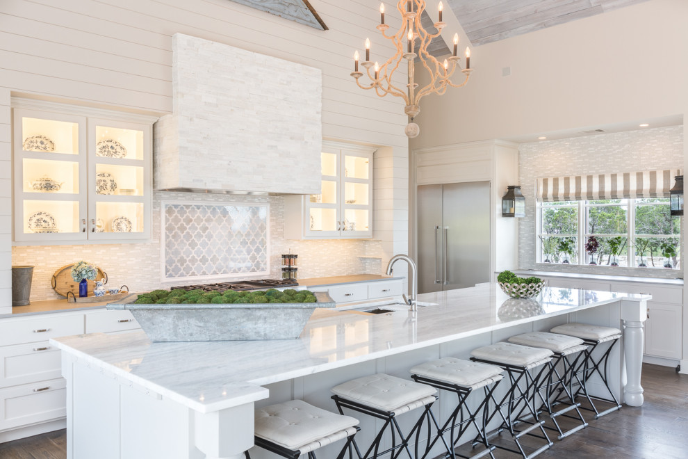 This is an example of a large farmhouse galley kitchen in Austin with a submerged sink, shaker cabinets, white cabinets, white splashback, matchstick tiled splashback, stainless steel appliances, medium hardwood flooring, an island, brown floors and white worktops.