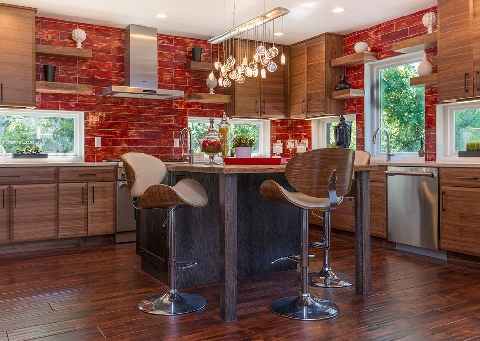 Cette image montre une cuisine design en L et bois foncé avec un placard avec porte à panneau surélevé, une crédence rouge, un électroménager en acier inoxydable, parquet foncé et îlot.