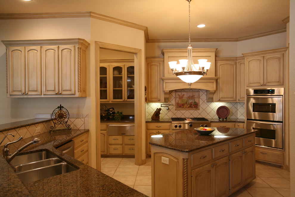 Example of a classic ceramic tile eat-in kitchen design in Austin with a triple-bowl sink, raised-panel cabinets, beige cabinets, granite countertops, beige backsplash, ceramic backsplash, stainless steel appliances and an island