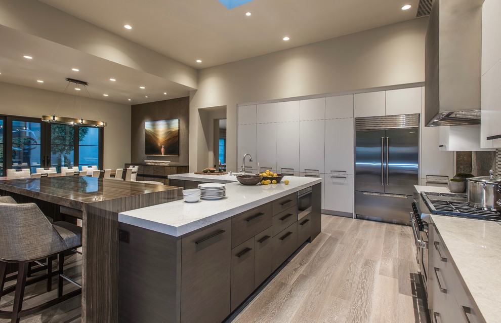 Design ideas for a contemporary u-shaped open plan kitchen in Phoenix with flat-panel cabinets, white cabinets, engineered stone countertops, green splashback, slate splashback, stainless steel appliances, light hardwood flooring, multiple islands, beige floors and white worktops.