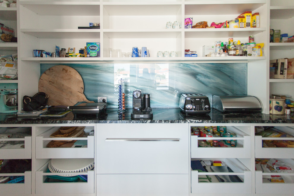 This is an example of a contemporary single-wall kitchen pantry in Gold Coast - Tweed with a submerged sink, flat-panel cabinets, white cabinets, marble worktops, blue splashback, glass sheet splashback, stainless steel appliances, medium hardwood flooring and an island.