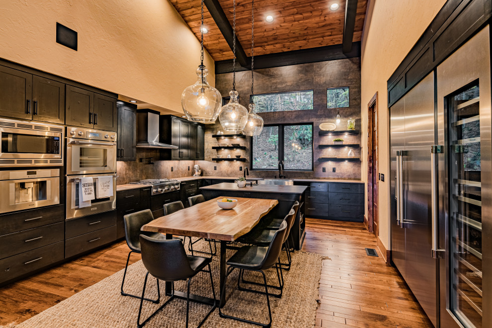 Inspiration for a large rustic galley medium tone wood floor and brown floor open concept kitchen remodel in Atlanta with a farmhouse sink, flat-panel cabinets, black cabinets, solid surface countertops, multicolored backsplash, stone slab backsplash, stainless steel appliances, an island and multicolored countertops