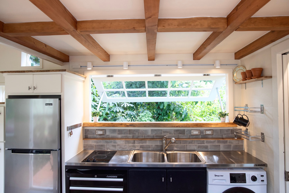 Foto på ett litet maritimt grå kök, med en dubbel diskho, släta luckor, svarta skåp, bänkskiva i rostfritt stål, grått stänkskydd, stänkskydd i keramik, rostfria vitvaror, laminatgolv och en köksö