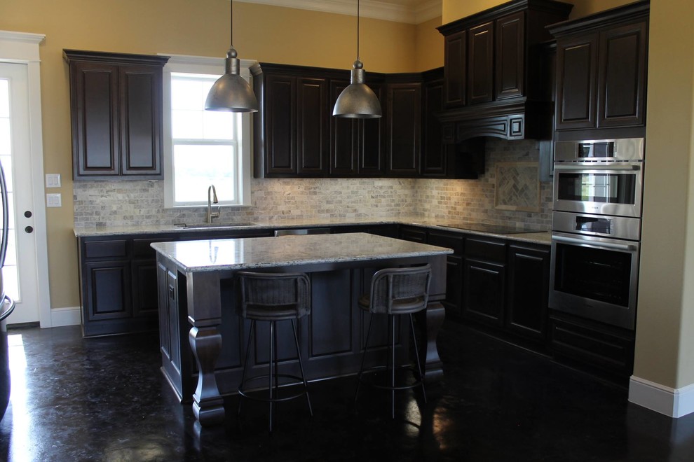Exempel på ett lantligt kök, med en enkel diskho, luckor med upphöjd panel, skåp i mörkt trä, granitbänkskiva, grått stänkskydd, stänkskydd i stenkakel, rostfria vitvaror, betonggolv och en köksö